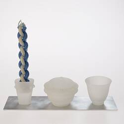 Opaque glass set on metal tray. Candle holder with woven blue white candle, lidded spice container and cup.