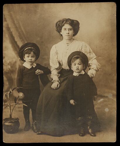 Seated woman poses with two standing young boys in studio setting.