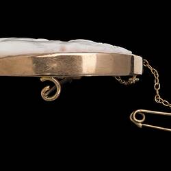 Profile of oval white brooch with cameo in gold setting with safety chain. Horizontal bar.
