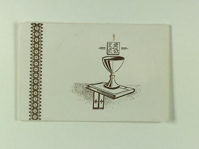 Front of glossy white, single-fold card with embossed gold illustrations of a cup on a book, with what appears to be a ribbon or eccesiastical stole underneath.