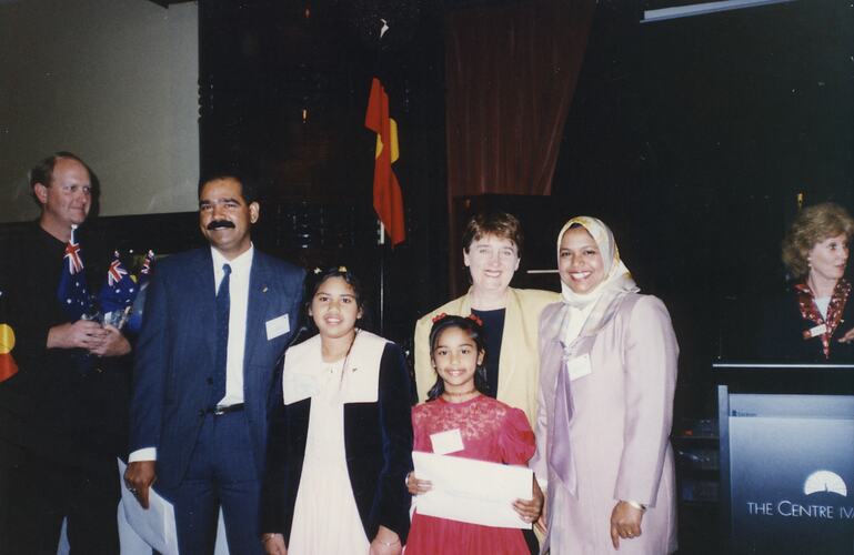 Man, woman and two girls pose with another woman. The girl holds a certificate. Man at left holds small Austra