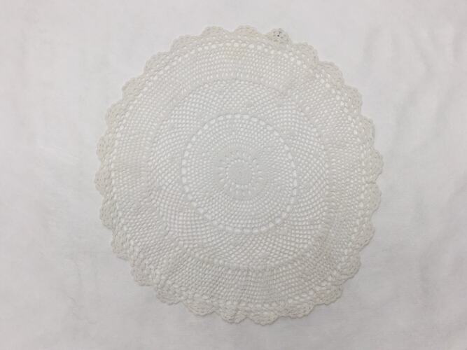 White cotton crochet doily round with scalloped edges.