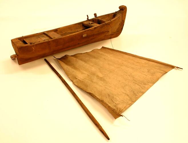 A wooden model boat with sail and pole.