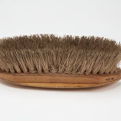 Oval shaped light brown wooden brush with off-white bristles.