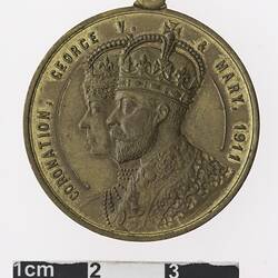 Round gold coloured medal with profile of a crowned man and woman, text surrounding.