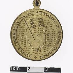 Round medal with map of Tasmania with flag, with text surrounding.