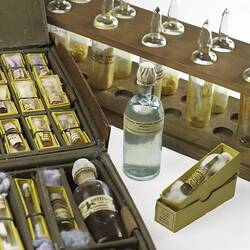 Labelled glass ampoules containing liquid. Stored upright in wooden rack and packed individually in a case.