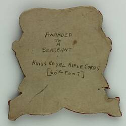 Back of badge showing writing on paper.