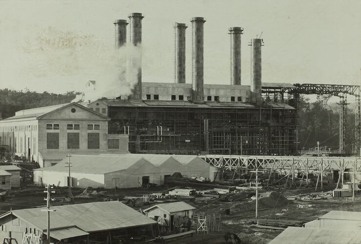 Six chimneys on top of a boiler house. Shed-like buildings in foreground.