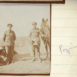 Two men in military uniform, one holding a horse by its bridle.