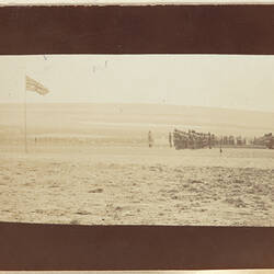 Rows of servicemen standing in formation on right, flag on left, hill in background.