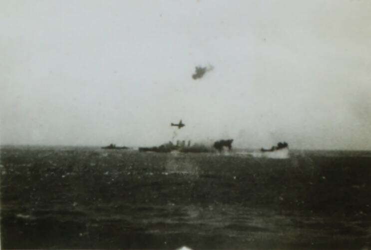 Ship surrounded by explosions in background, an aeroplane is in the air above it.