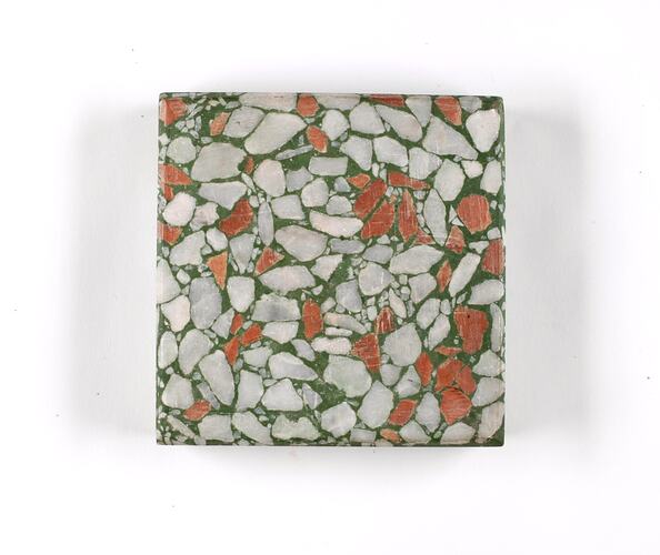 Square terrazzo sample with green base and white and ochre coloured aggregate.