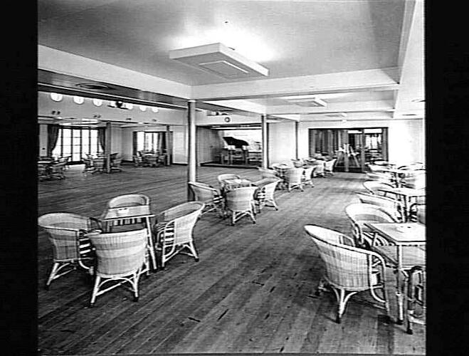 Ship interior. Open dancing space. Round cane chairs and square tables around edge of room.
