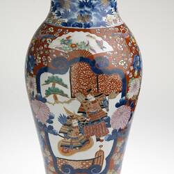 Ornate colourful vase, slightly tapered body with a small lip. Off-white base with two Shogun figures amongst peonies, cherry blossoms, chrysanthemums, fans and butterflies.