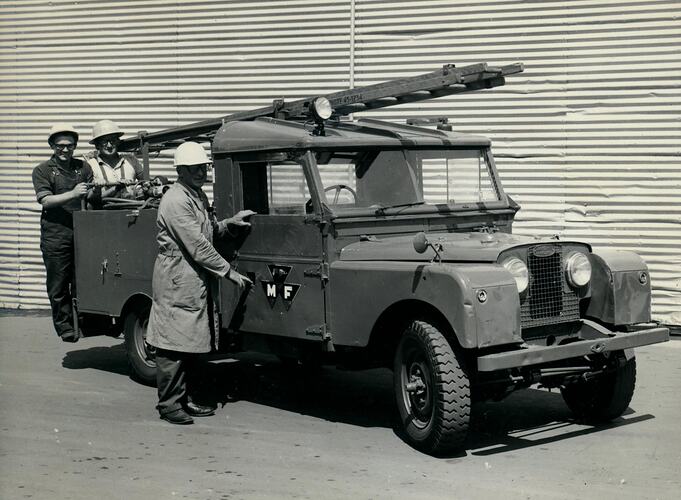 Three men stand beside a Land Rover with ladder on roof.