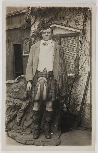 Portrait of a man posing behind a life-sized figurine dressed in traditional Scottish costume with no head.