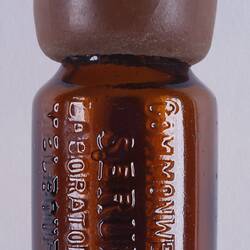 Round brown glass bottle with brown rubber lid. Raised lettering on outside.