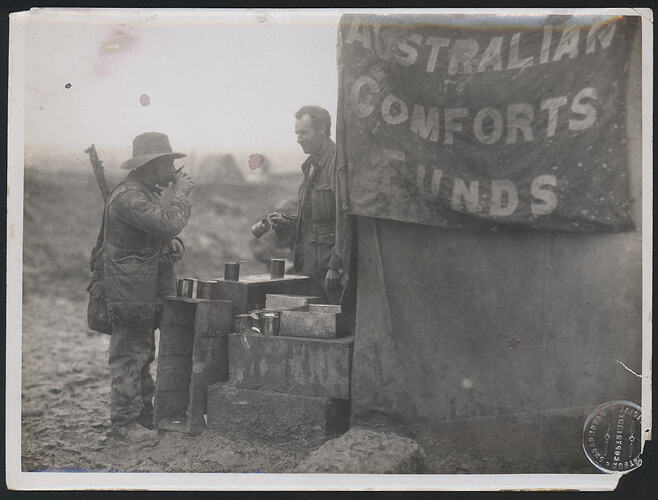 A soldier standing in front of buffet drinking from a cup.
