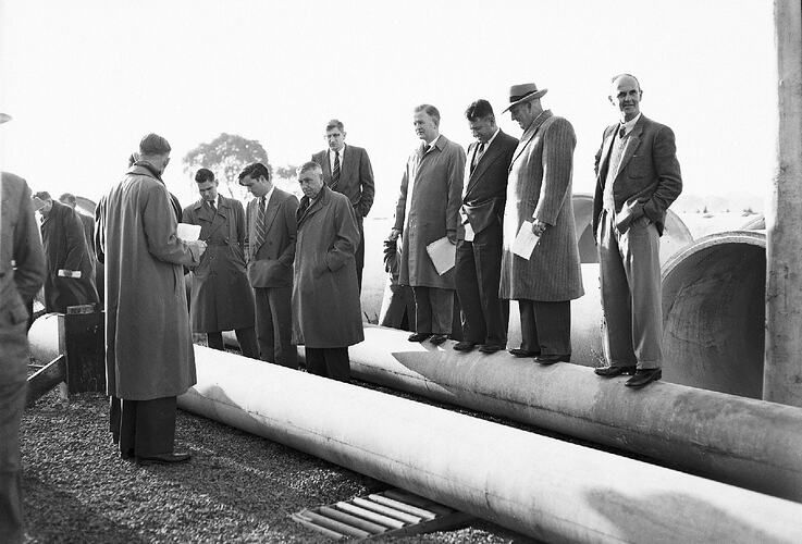 Monochrome photograph of men testing cement pipes.