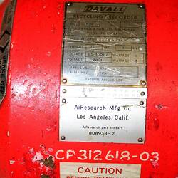 Bright orange-red metal cylindrical casing with domed ends, plates and labels. Two cords fixed at ends. Detail.