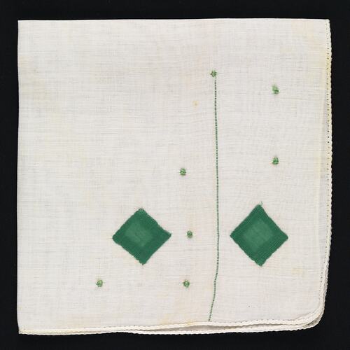 Folded handkerchief with green embroidered diamonds.