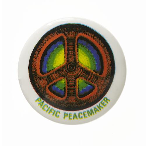 White badge with orange and black peace symbol. Blue, green and yellow within. Green text below.