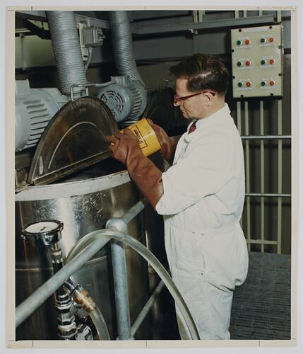 Man pouring contents of tin into metal tank.