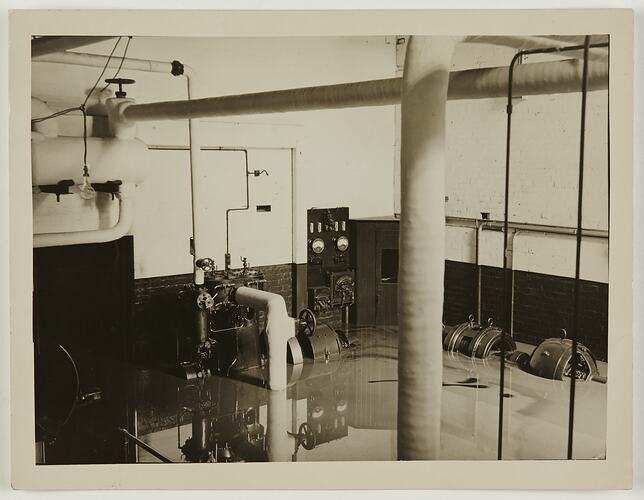 Generators under water. At left are large pipes and a light bulb hanging from the ceiling.