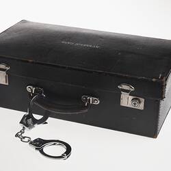 Black leather briefcase marked 'Attache Case' with handcuffs on the handle.