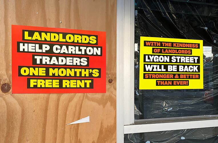 Two posters. Red one on timber has printed yellow/white text. Yellow one on window printed red/white text.