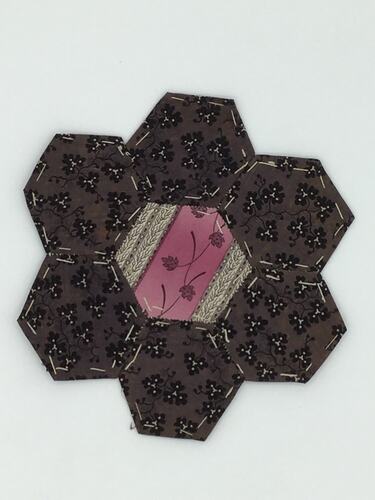 Grey hexagonal coloured fabric patches that are stitched together. Pink centre.