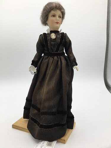 A doll dressed in a dark brown dress with a cameo brooch
