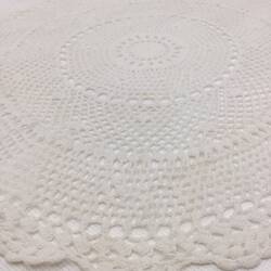Detail of white cotton crochet doily round with scalloped edges.