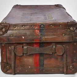 Side view of worn brown leather suitcase with handle. Faded red and black stripe.