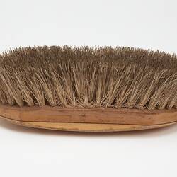 Oval shaped light brown wooden brush with off-white bristles.