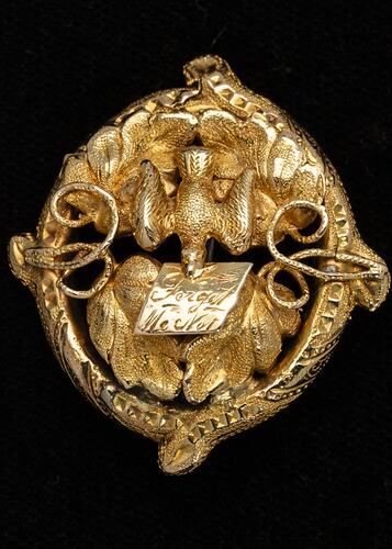 Round gold decorative brooch with bird holding note in its beak.