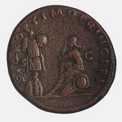 Round coin with figure sitting on shield facing trophy at left. Text around.