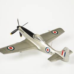 Back view of silver model plane. Blue, white, red roundel on sides and wings. Red, white, blue flag on tail. Front black four blade propeller.