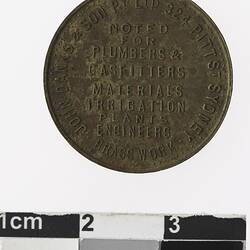Round medal with eight lines of text in centre, and text surrounding.