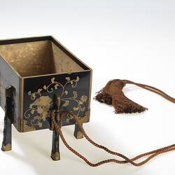 Decorated, four-legged box tied with tassles, no lid.