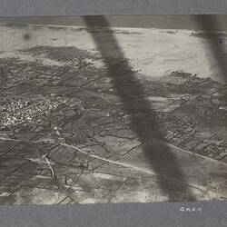 Aerial view of city and surrounding land with coastline along top, two long shadows across image.