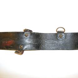 Leather belt with gold coloured metal hook, two metal rings attached to edge of belt, close-up view.