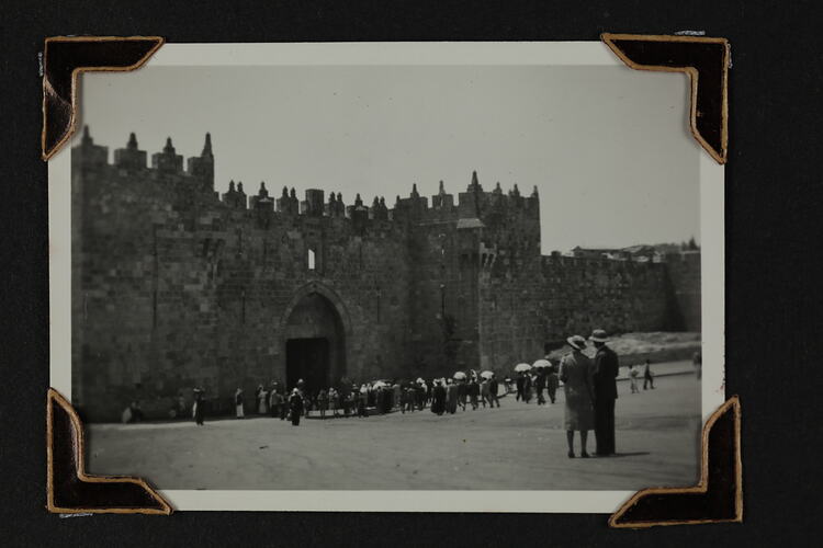 Crowd of people standing by an entranceway in a large stone wall.