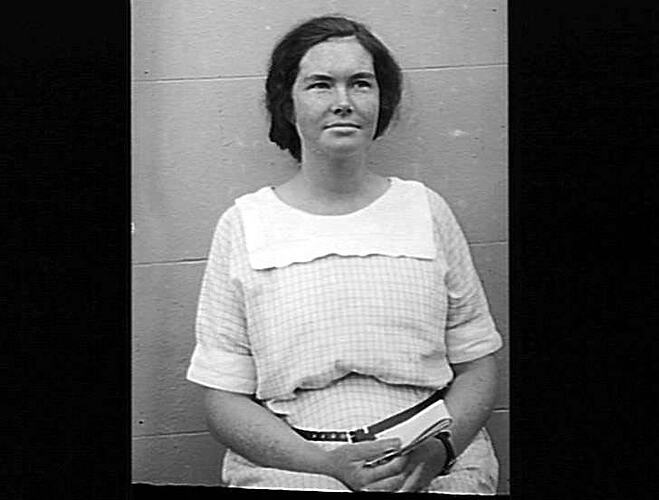 Seated woman in pale checked dress.