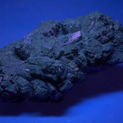 Dark mineral specimen lit with purple light.