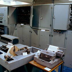 Grey metal cabinets, gauges, circuitry, typewriter, machinery.
