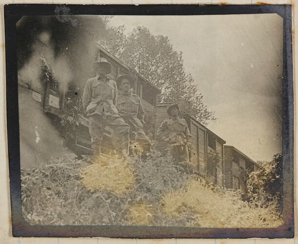 Three soldiers standing in front of a stationary train.