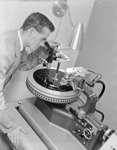 Man looking into microscope at record on disc-shaped equipment.