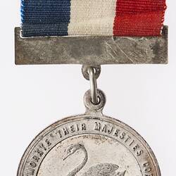 Round silver coloured medal with swan and text surrounding, blue, white and red ribbon attached.